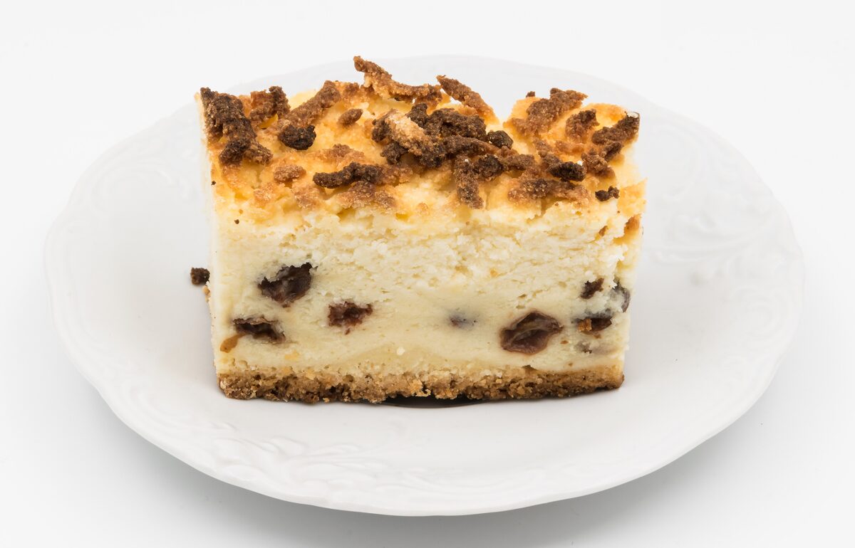 A slice of Polish cheesecake with raisins and a crumble top on a white plate