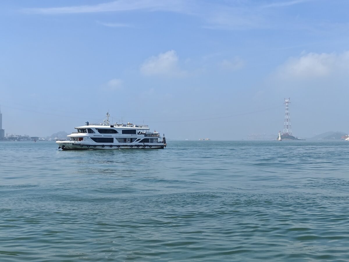 A white passenger ferry crossing Xiamen harbor under a blue sky