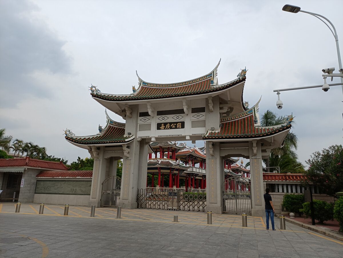 The stone gateway of Jiageng Park (Kah Kee Park) in Jimei, with tiered, upswept tiled roofs, and a red pavilion behind it