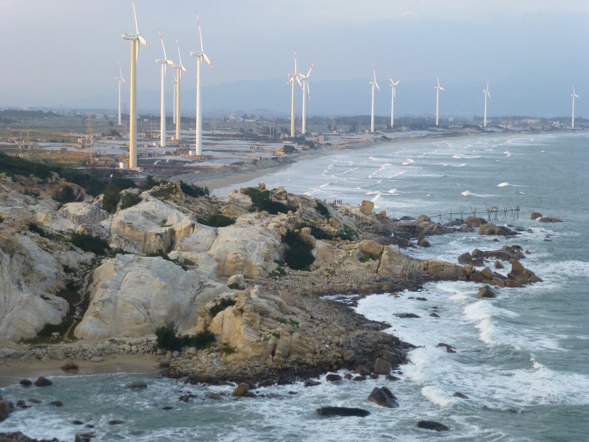 Wind turbines along the shore beyond a rocky coast with surf on the Liu'ao Peninsula