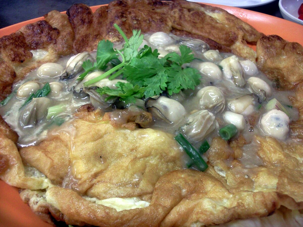 A plate of oyster omelette, the Teochew version, with small oysters in a glossy sauce over the egg and a sprig of coriander on top