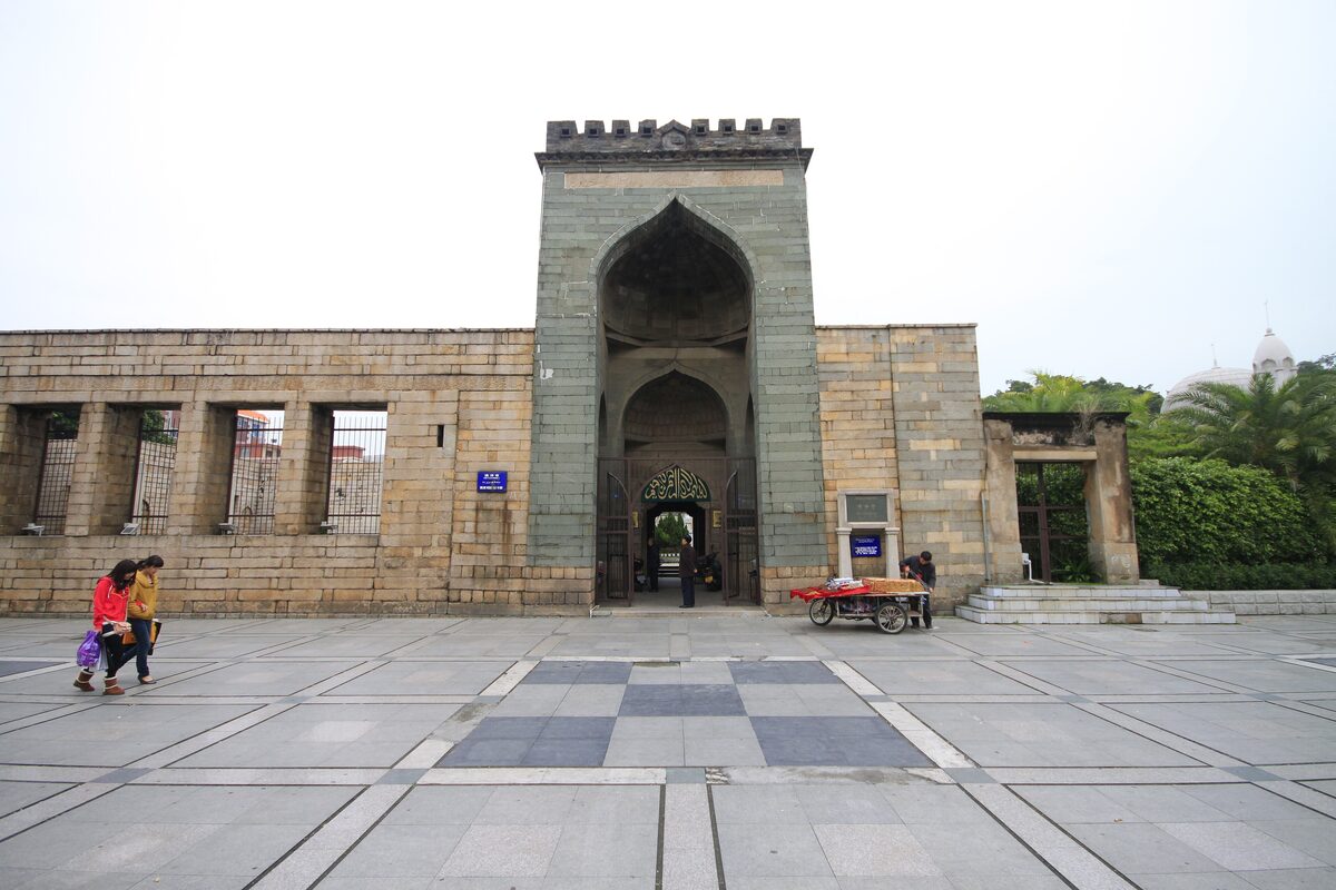 The weathered granite gateway of Qingjing Mosque with its tall pointed arch, across a paved square