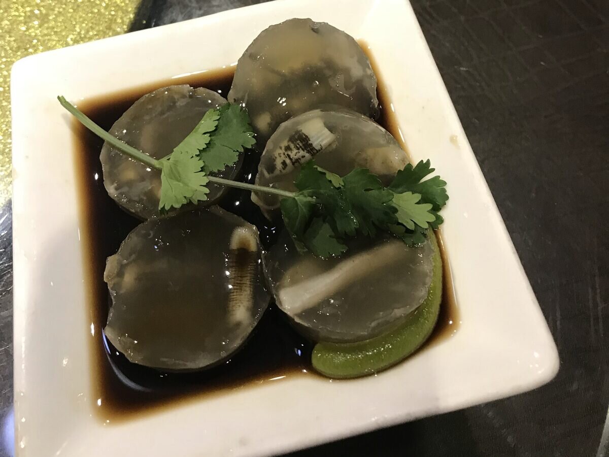 Rounds of clear sea worm jelly with the worms visible inside, in a white dish of dark soy sauce with coriander and a lime wedge