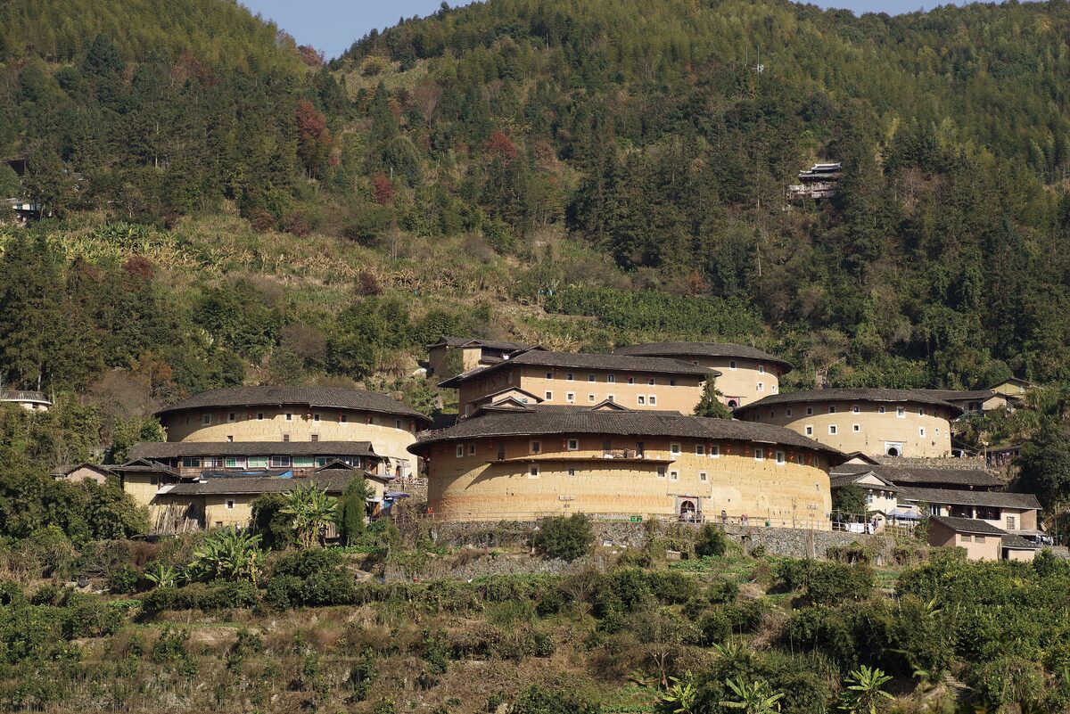 The earthen buildings of the Tianluokeng cluster on their hillside, with a forested ridge behind