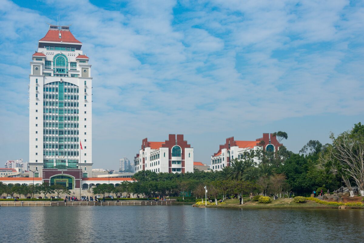 The Jiageng Complex towers beside Furong Lake on the Xiamen University campus, under a blue sky with clouds