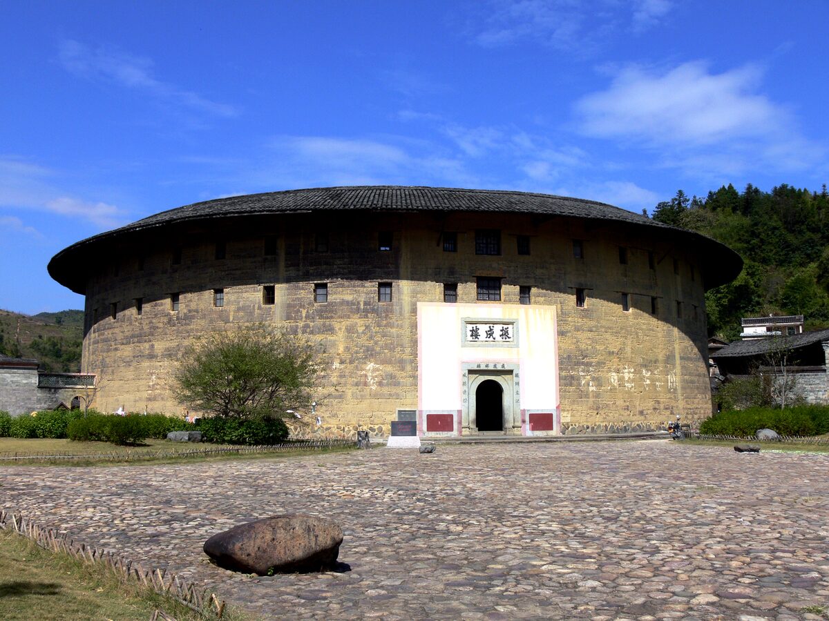 Zhenchenglou in Hongkeng, a large round tulou with a wide tiled roof and a white gateway, under a blue sky