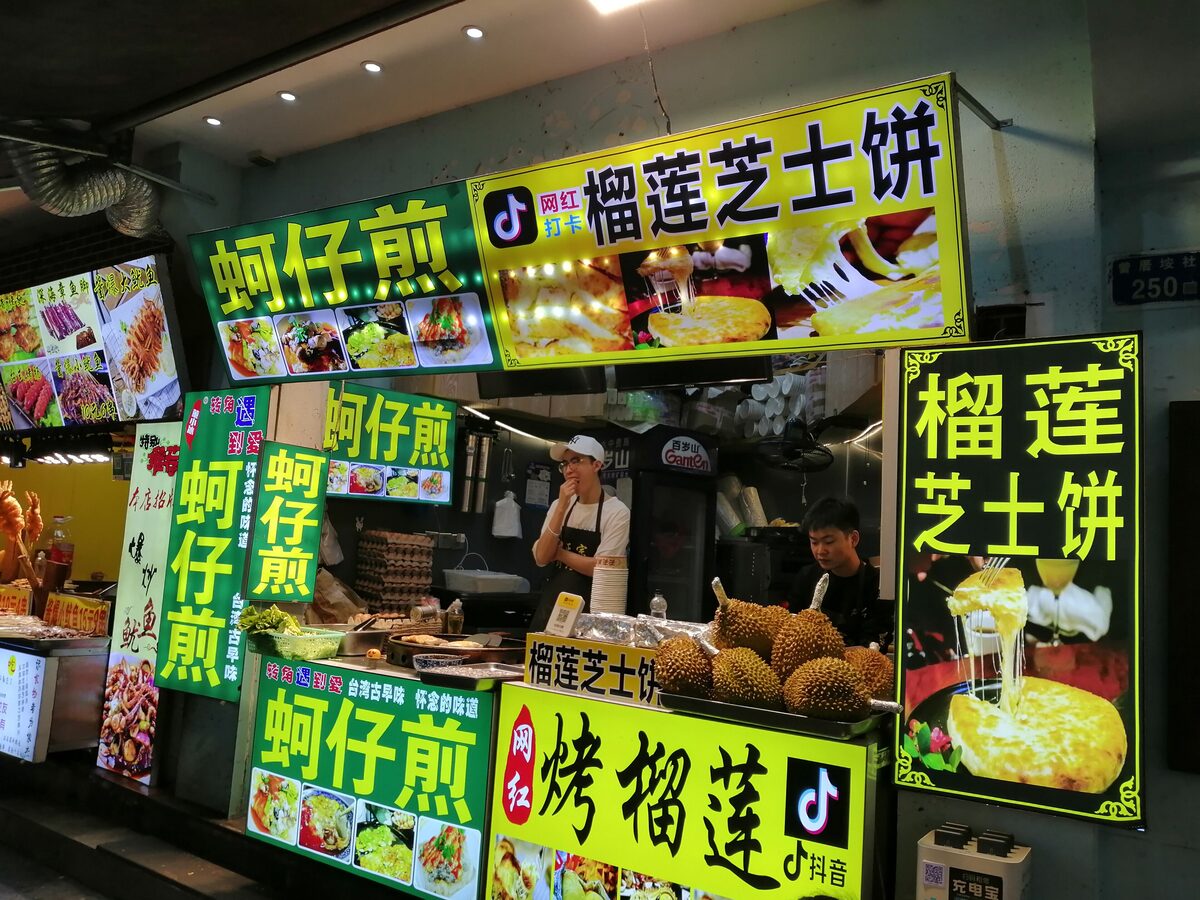 A brightly lit oyster omelette stall in Zengcuoan, with signs above the counter and cooks at work