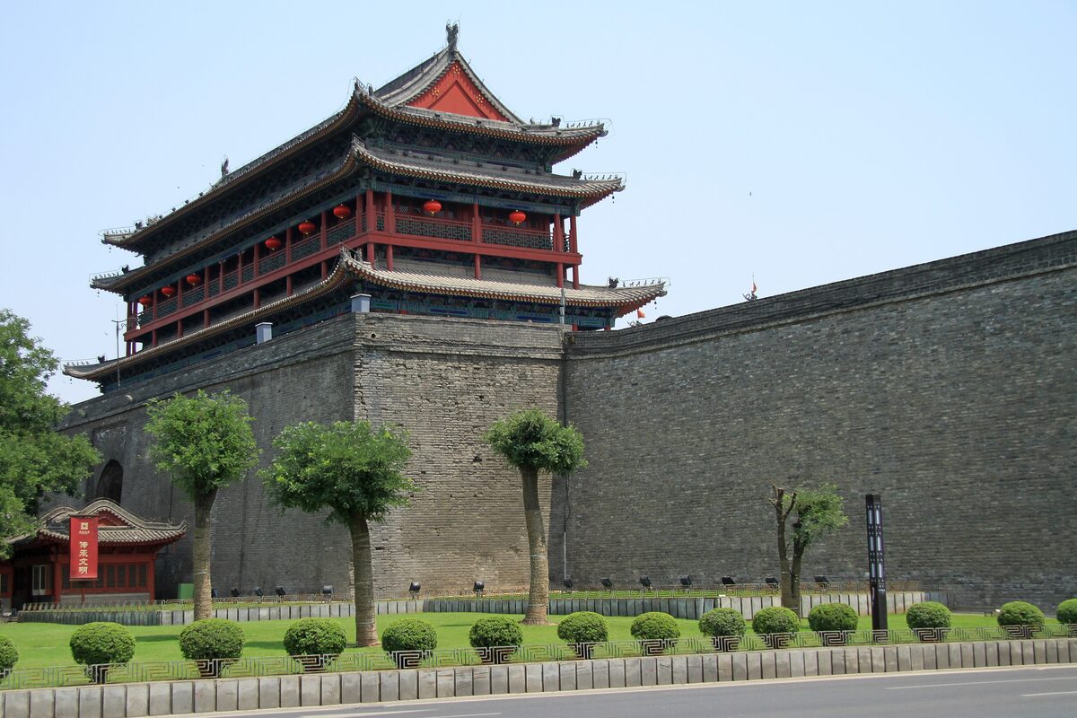 A red-roofed gate tower rising above the grey brick Xi'an City Wall on a clear day, with a strip of clipped lawn below