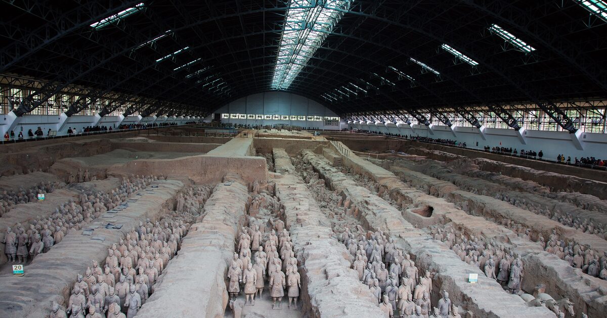 Rows of clay warriors standing in the long earth trenches of Pit 1 of the Terracotta Army, under the huge arched hangar roof