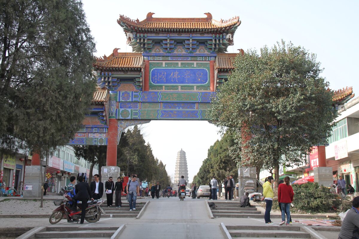 A painted paifang arch at the end of a street, with the Famen Temple pagoda in the distance beyond it