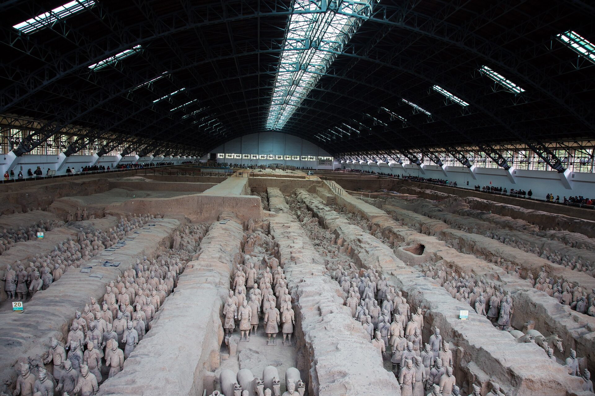 Rows of clay warriors standing in the long earth trenches of Pit 1 of the Terracotta Army, under the huge arched hangar roof