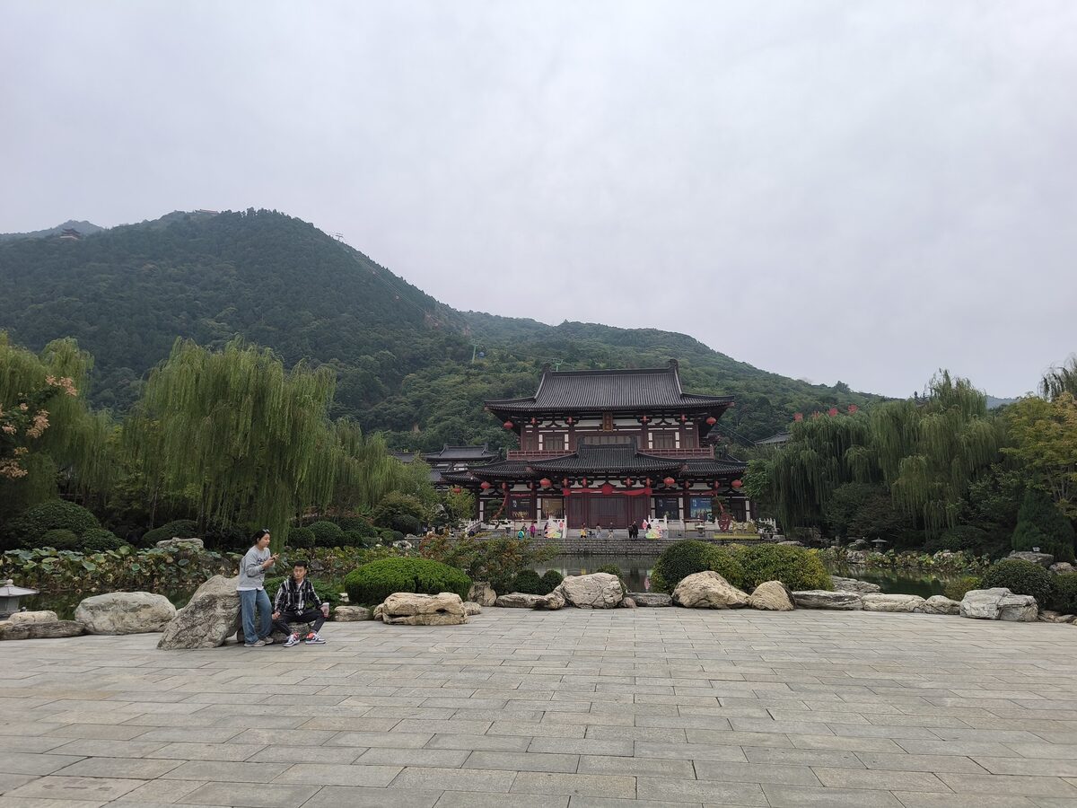 Changsheng Hall at Huaqing Palace across a stone-paved square, with the wooded slopes of Mount Li behind it
