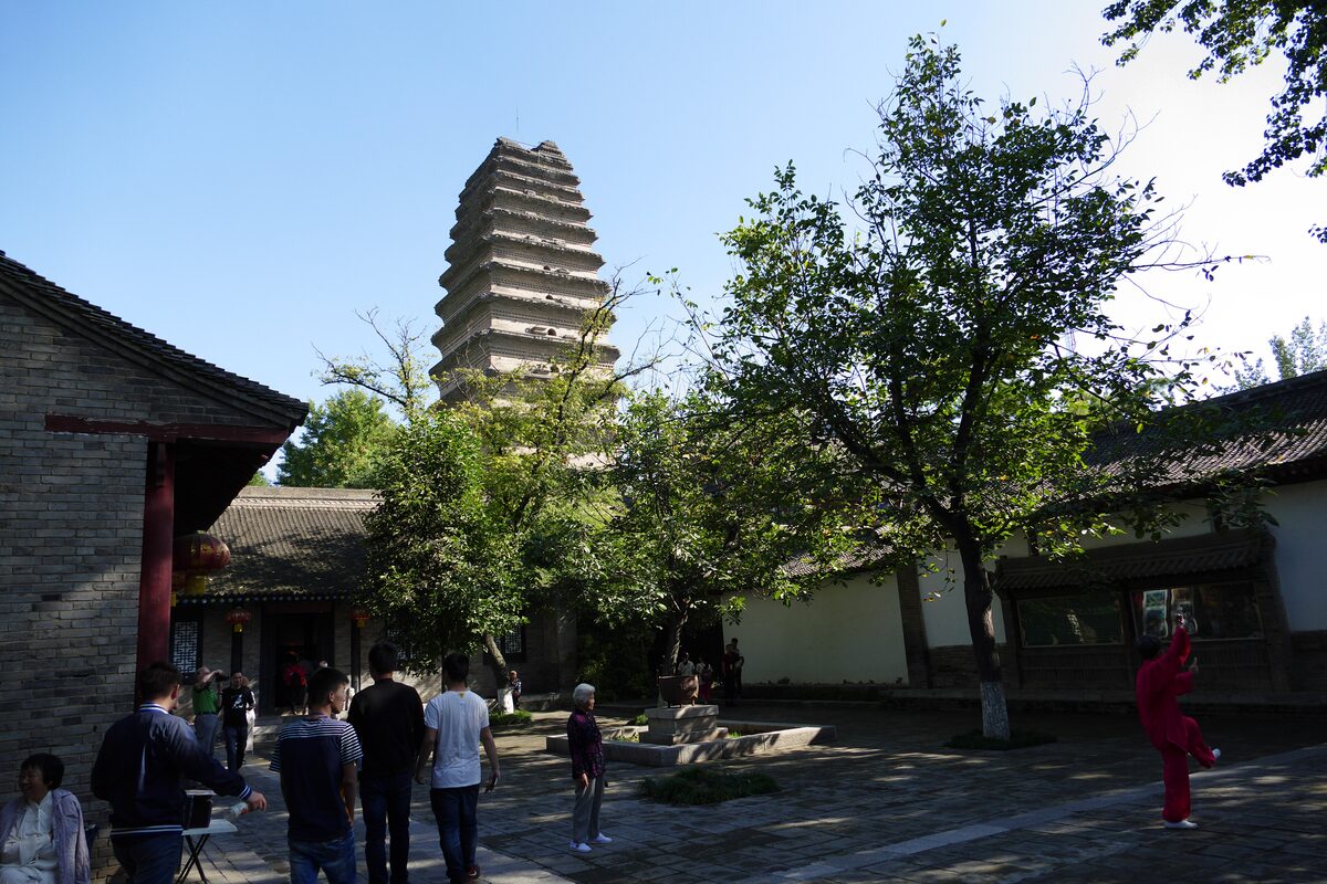 The Little Wild Goose Pagoda rising above trees in the courtyard of Jianfu Temple on a clear day, with visitors in the foreground