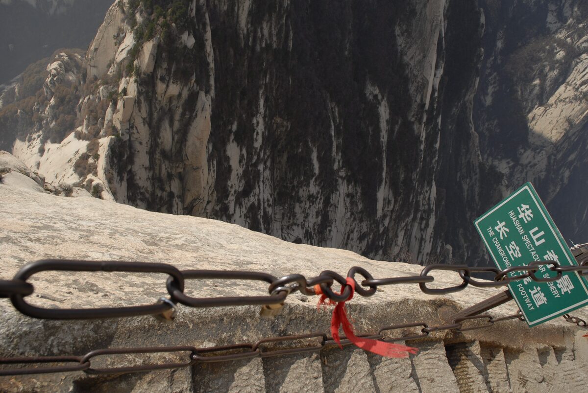 An iron safety chain and a narrow rock ledge on Mount Hua's Changkong plank walk beside a sheer cliff