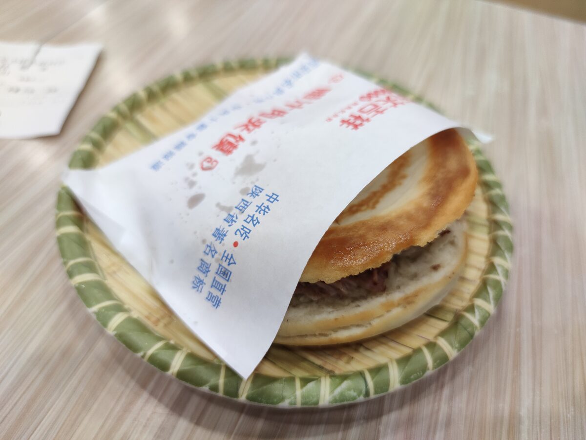 A roujiamo, a flatbread sandwich of braised pork, in its paper wrapper on a bamboo tray