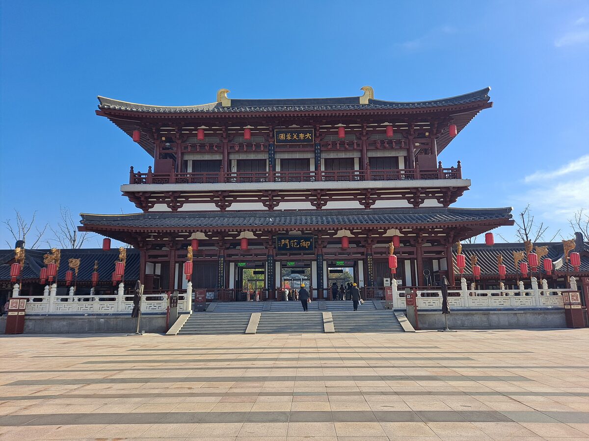 The two-storey red-pillared entrance hall of Tang Paradise, hung with red lanterns, seen across a wide paved plaza under a blue sky