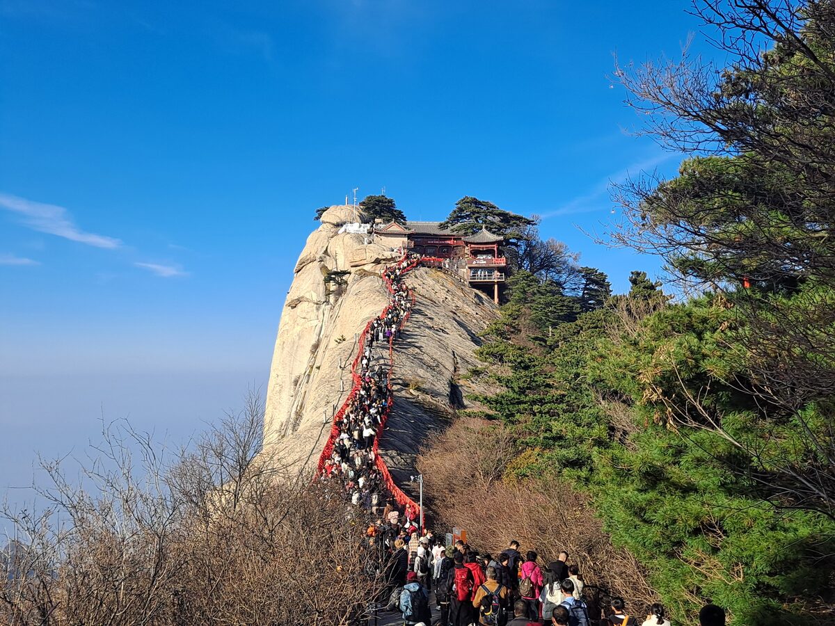 A line of climbers on the steps along a ridge leading up to a pavilion on Mount Hua's West Peak