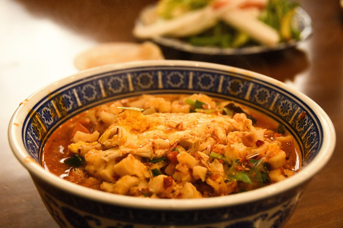 A blue-and-white bowl of yangrou paomo, lamb soup thick with torn flatbread, chili and herbs