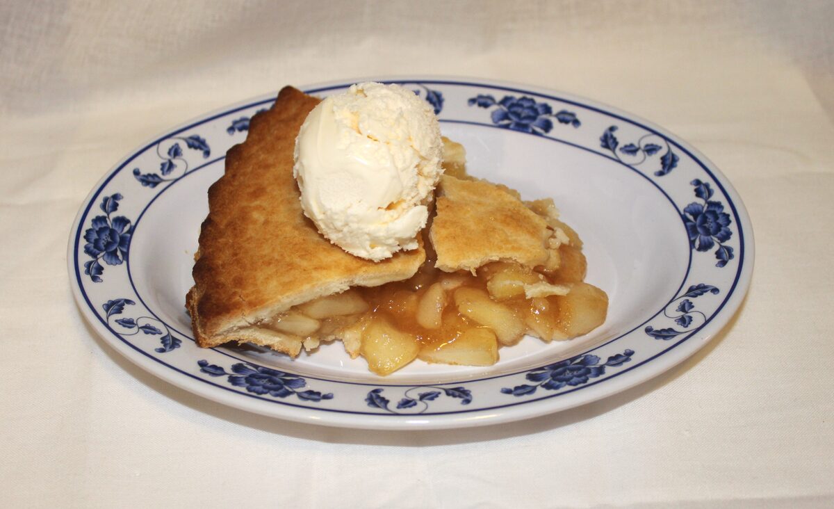 A slice of apple pie topped with vanilla ice cream
