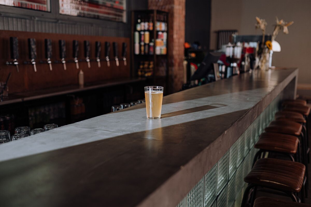 A pint of beer on a long taproom bar below a row of taps
