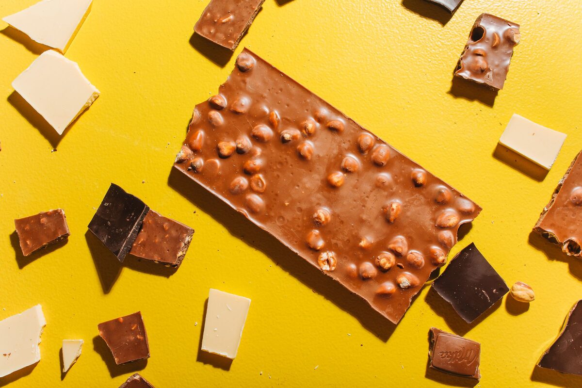 Pieces of milk, dark and white chocolate and a nut-studded chocolate bar on a yellow background