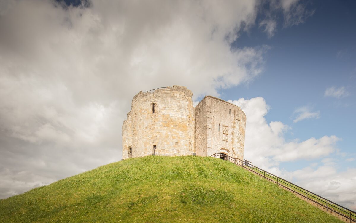 Clifford's Tower, a round stone keep on top of a steep grassy mound, with steps leading up to it