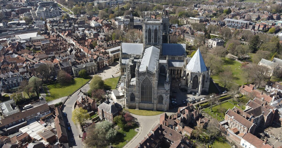 Aerial view of York Minster, its pale Gothic towers and lead roofs rising above the red-brick houses and green lawns of the old city