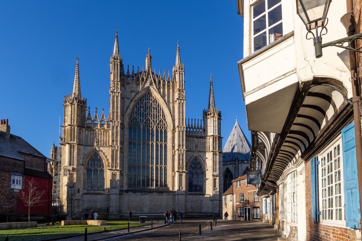 The west front of York Minster with its two Gothic towers and great window, seen from a lane of old houses