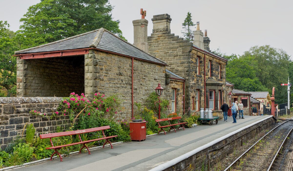 Goathland station on the North York Moors Railway, with a stone station building, flowers and red benches on the platform