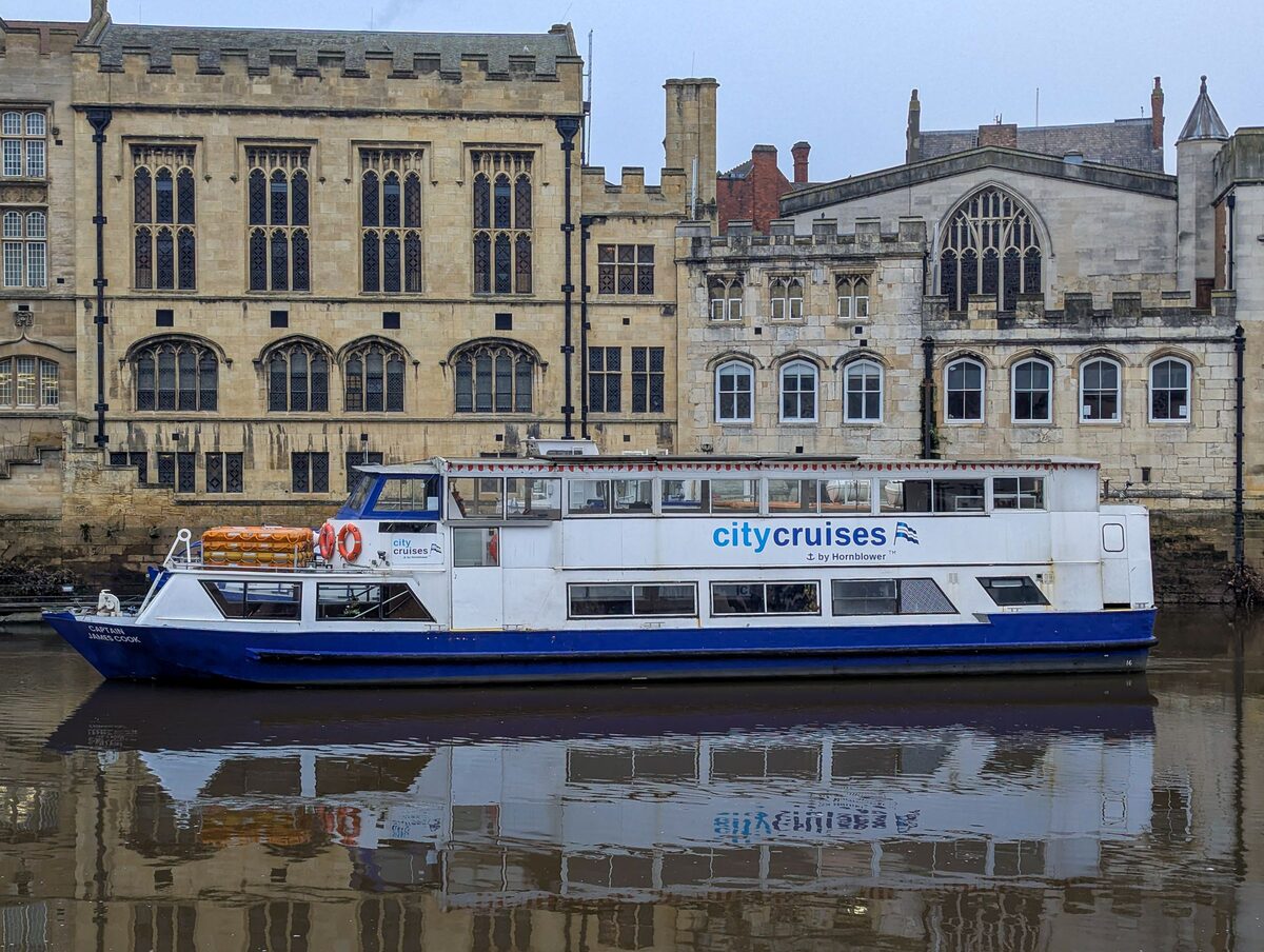 A City Cruises sightseeing boat moored on the River Ouse in York, in front of old stone buildings