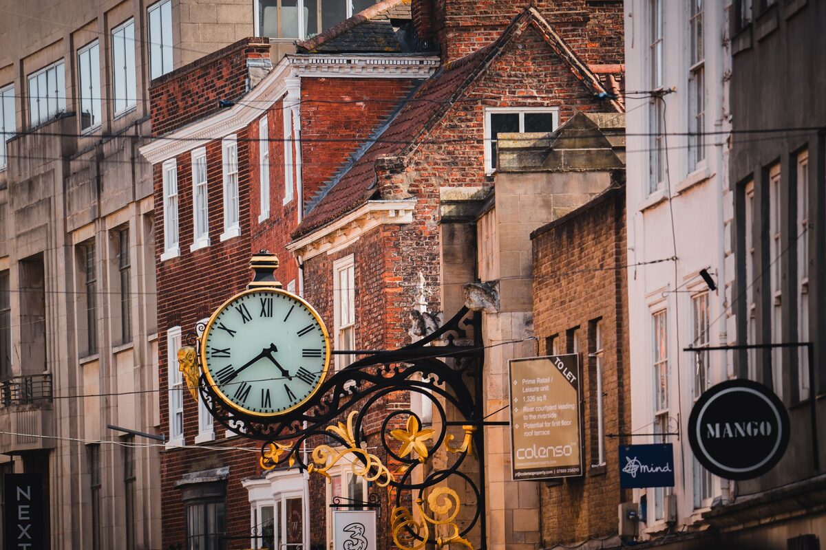 An ornate gilded clock hanging over Stonegate in York, among old brick and stone shopfronts