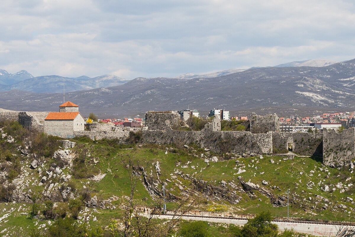 The ruined stone walls of the Bedem fortress on a hill above Nikšić, with the town's rooftops and snow-patched mountains behind