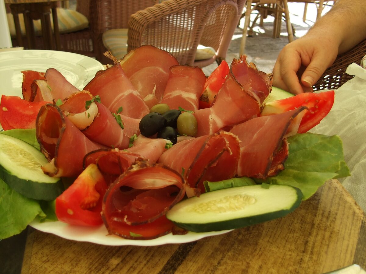 A plate of thinly sliced Njeguški pršut with tomato, cucumber, olives and lettuce