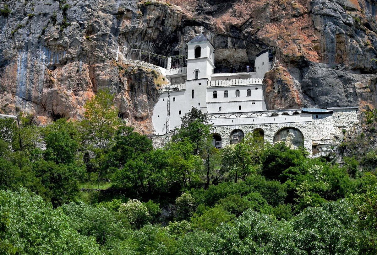 Ostrog Monastery, a white monastery built into a sheer rock cliff above green trees