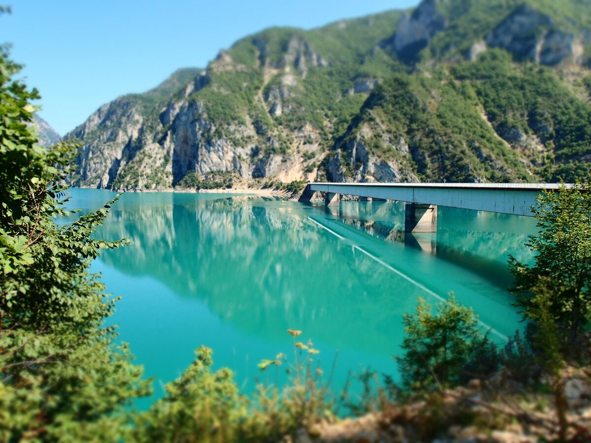 A turquoise reservoir between steep forested cliffs near Plužine, with a concrete bridge crossing the water