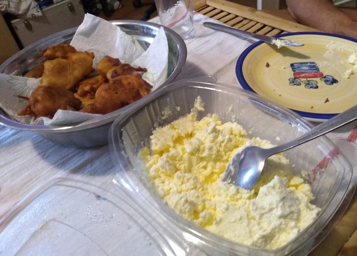 Priganice, small fried dough pieces in a metal bowl lined with paper, with a tub of fresh kajmak and a spoon beside them