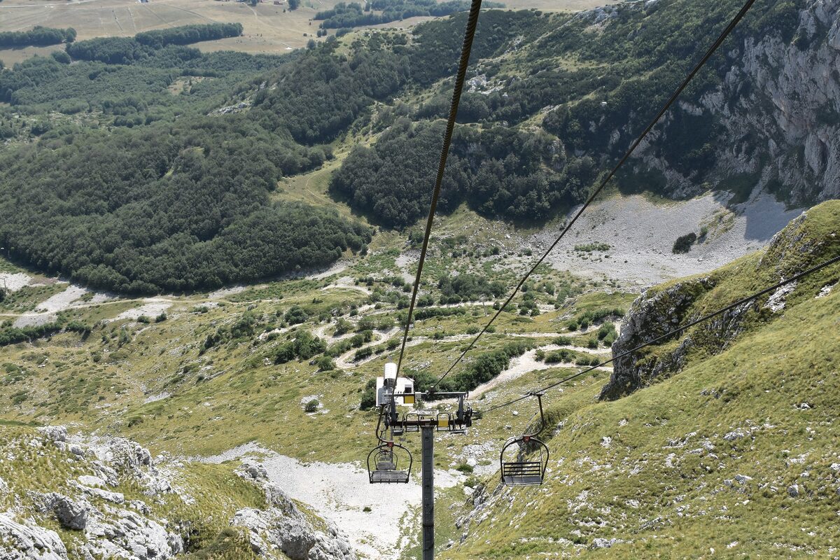 The Savin Kuk chairlift climbing a grassy slope in summer, with limestone outcrops and forest in the valley below