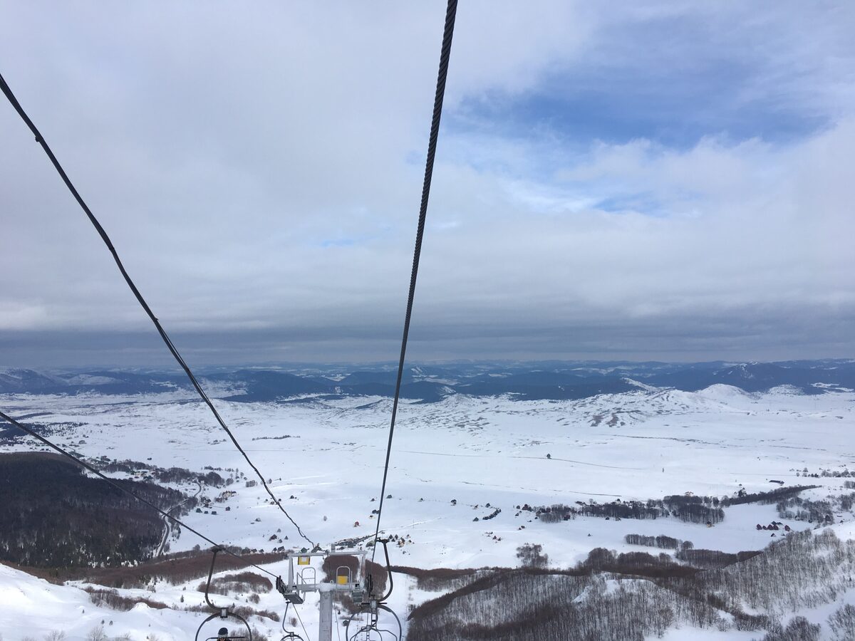 Winter view from a chairlift over the snow-covered plateau below the Savin Kuk ski area, with the lift cables and chairs in the foreground