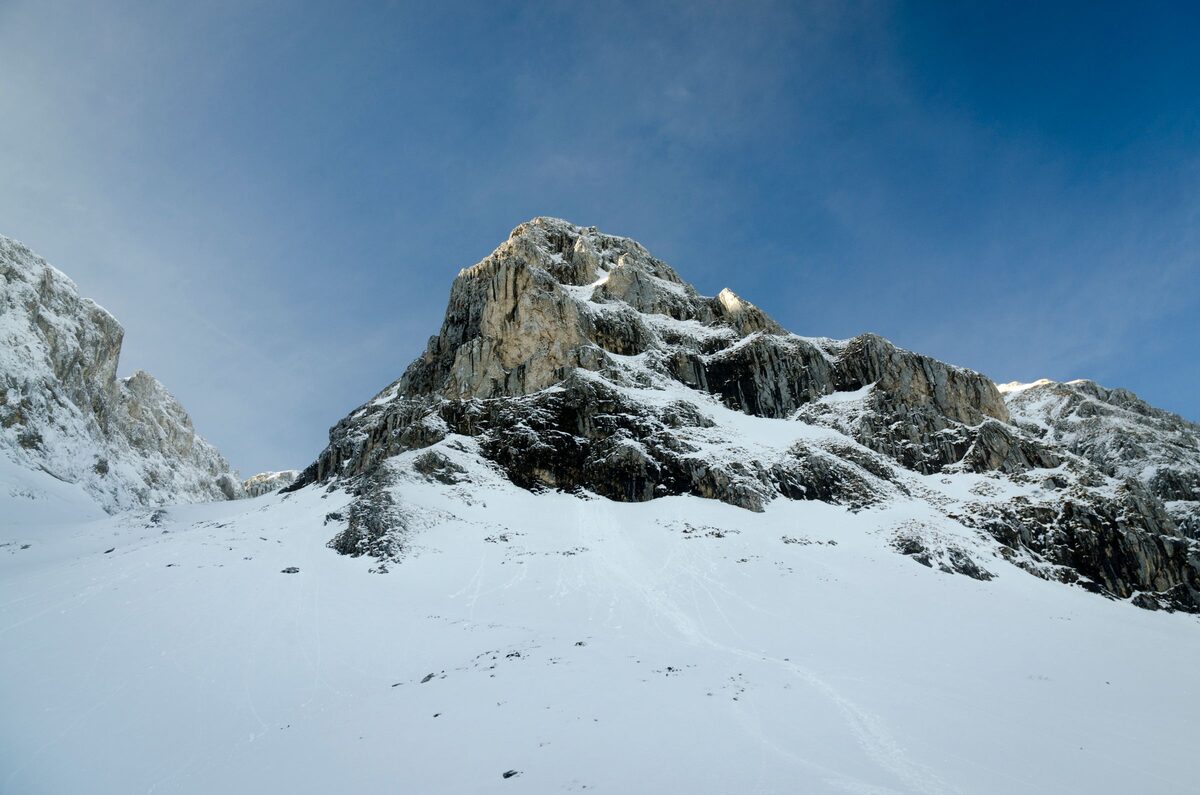 A snow-covered limestone peak against a deep blue winter sky, with an open snow slope in the foreground