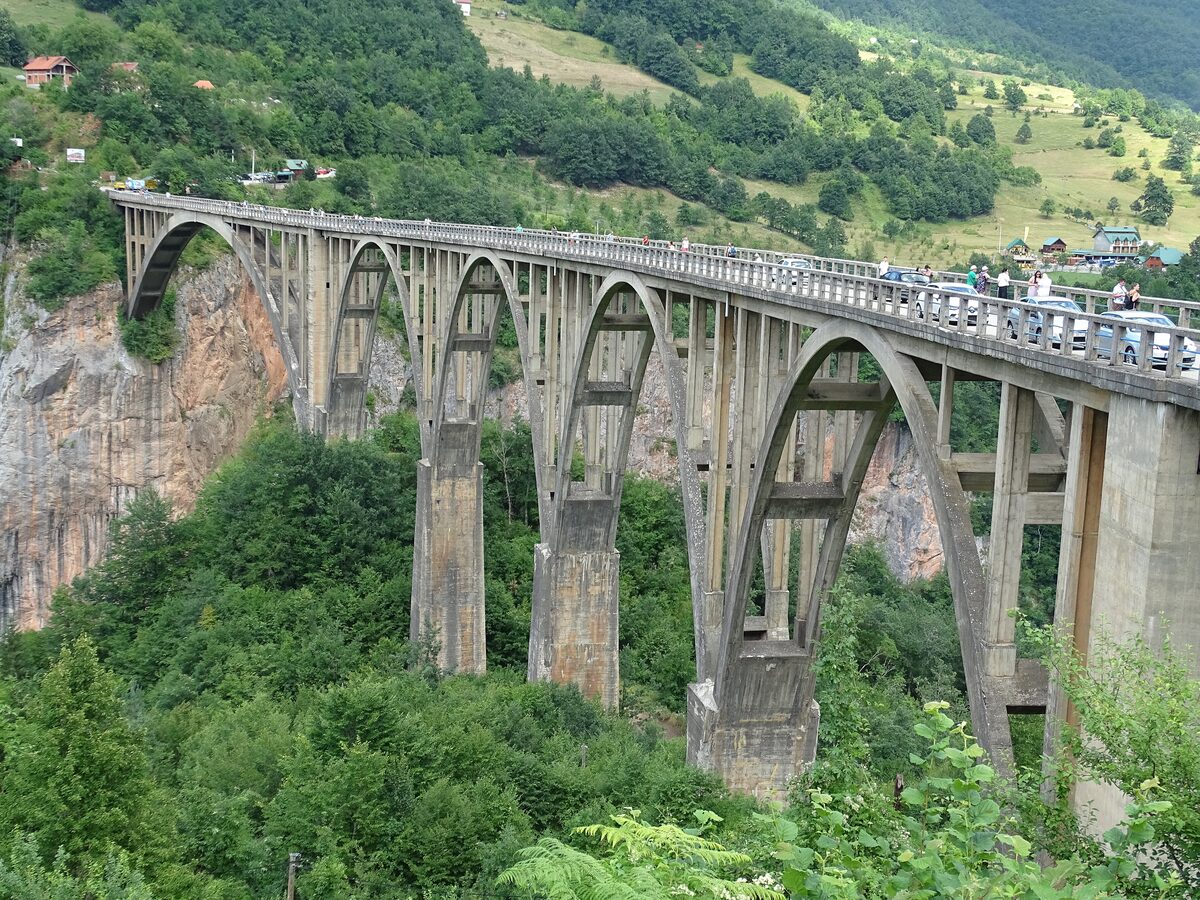 Đurđevića Tara Bridge, a long concrete arch across the Tara canyon with forest and a village on the slope beyond
