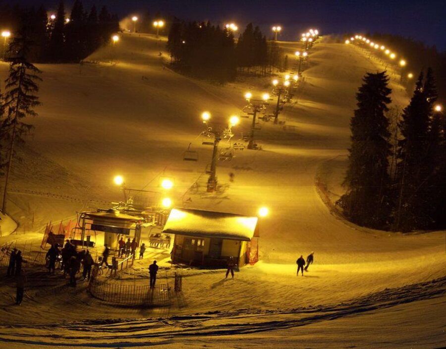The Kotelnica slope at Białka Tatrzańska at night, a floodlit piste with a lift station and skiers in the snow