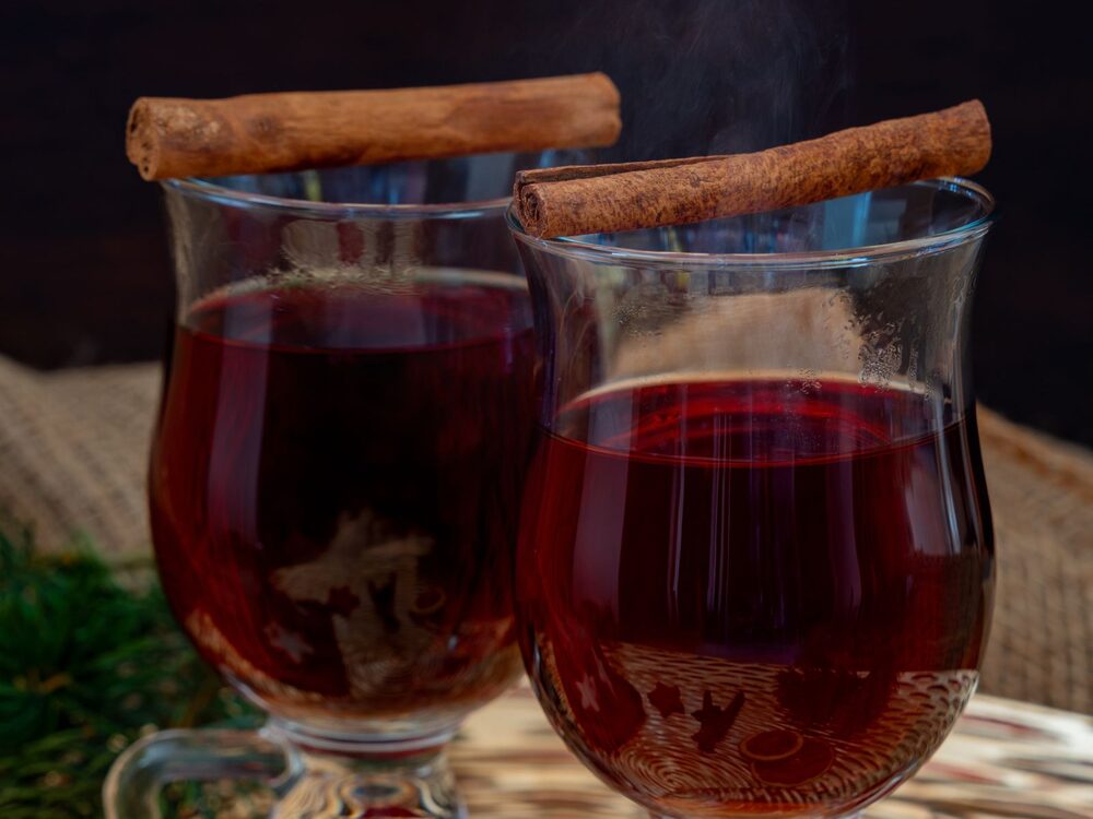 Two glasses of steaming mulled wine with cinnamon sticks, set against dark fir branches