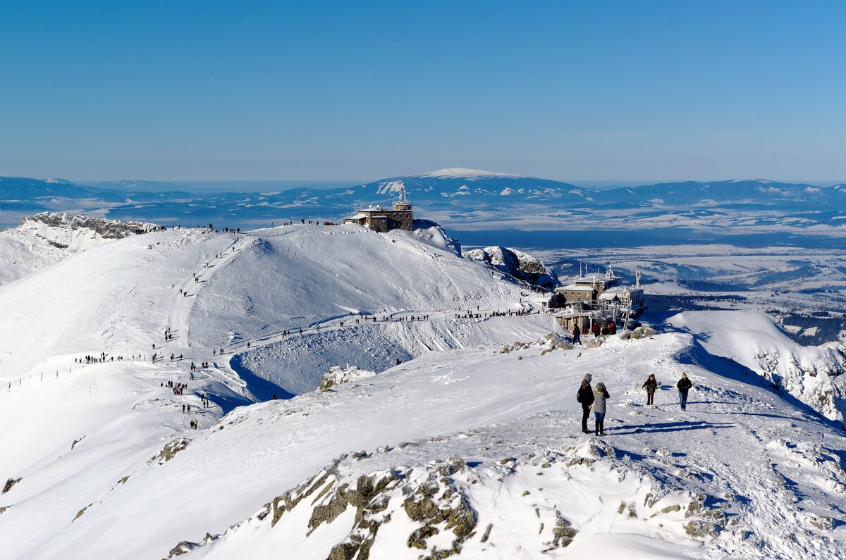 The snowy summit of Kasprowy Wierch on a clear winter day, with the observatory, the upper cable car station and walkers on the ridge