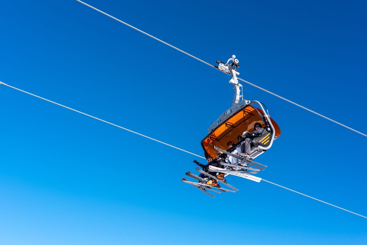 A chairlift with an orange bubble hood carrying skiers against a deep blue sky at Białka Tatrzańska