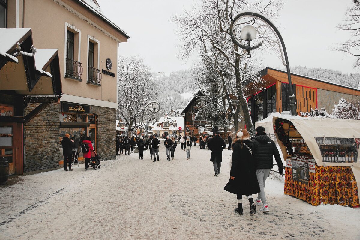 Krupówki in winter: a snowy pedestrian street with walkers, street lamps, a souvenir stall and wooden-roofed shops
