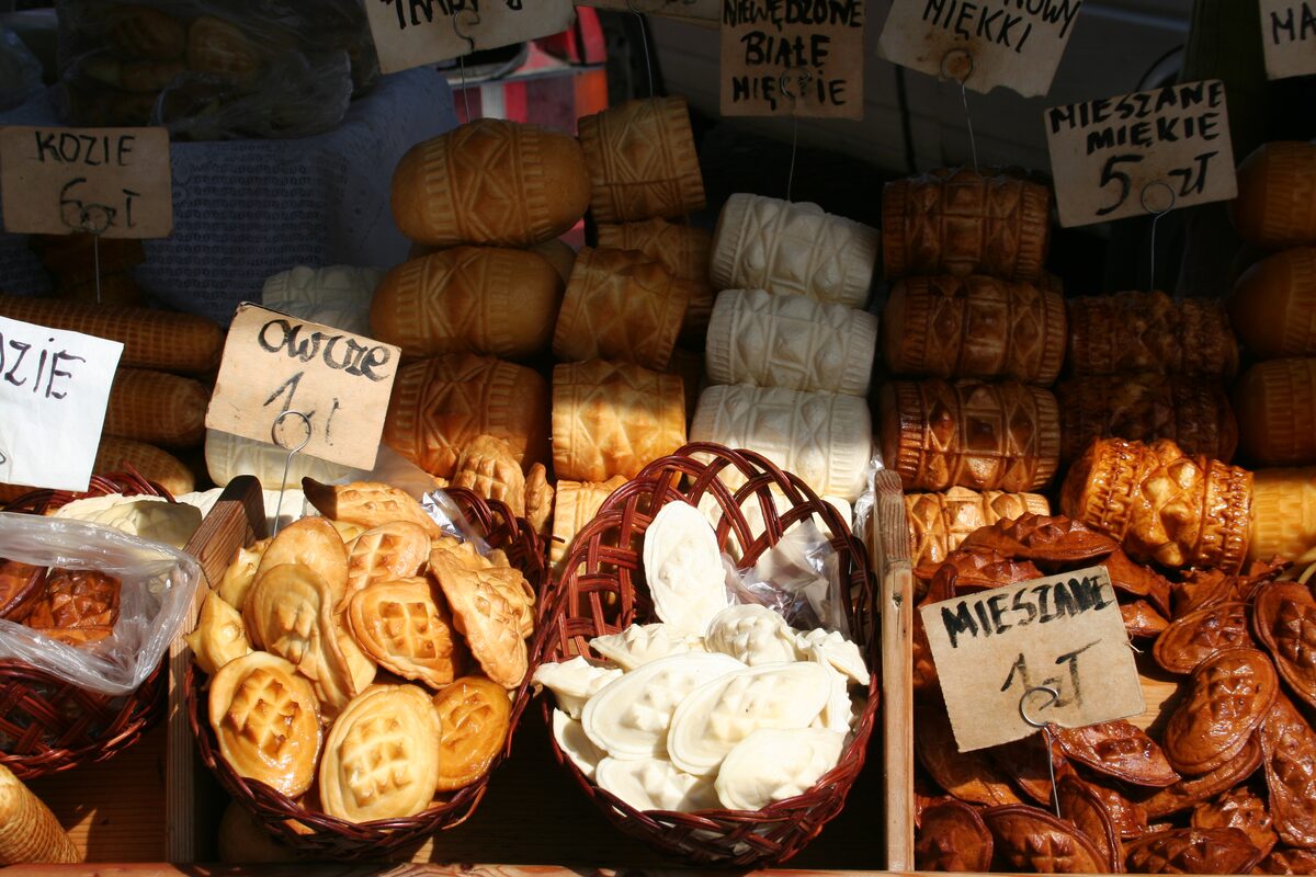 A market stall piled with smoked sheep's milk cheeses, spindle-shaped oscypki with patterned ends and baskets of small molded ones, with price tags