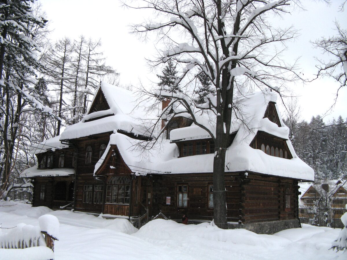Villa Koliba, a dark wooden villa in Zakopane style under deep snow, with a bare tree in front