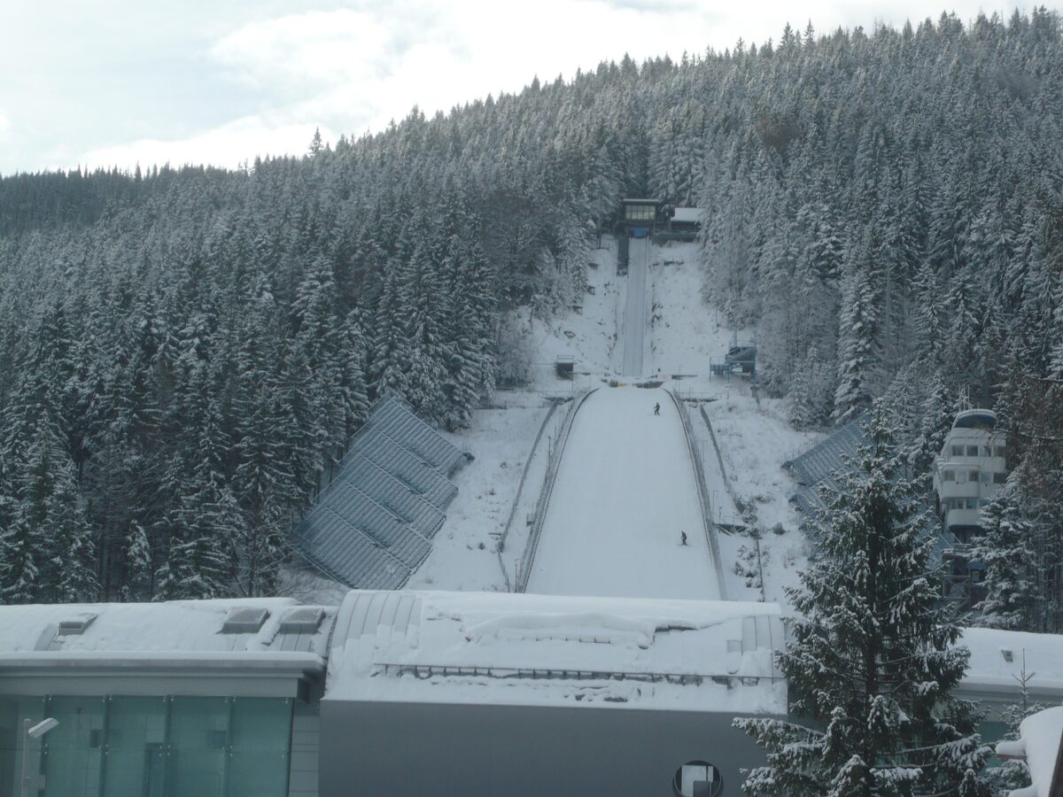 The Wielka Krokiew ski jump in snow, its landing hill and a skier on the run among snow-laden spruces