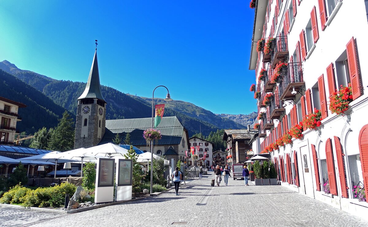 Bahnhofstrasse in Zermatt in summer, a pedestrian street with red-shuttered hotels and the church spire at the end