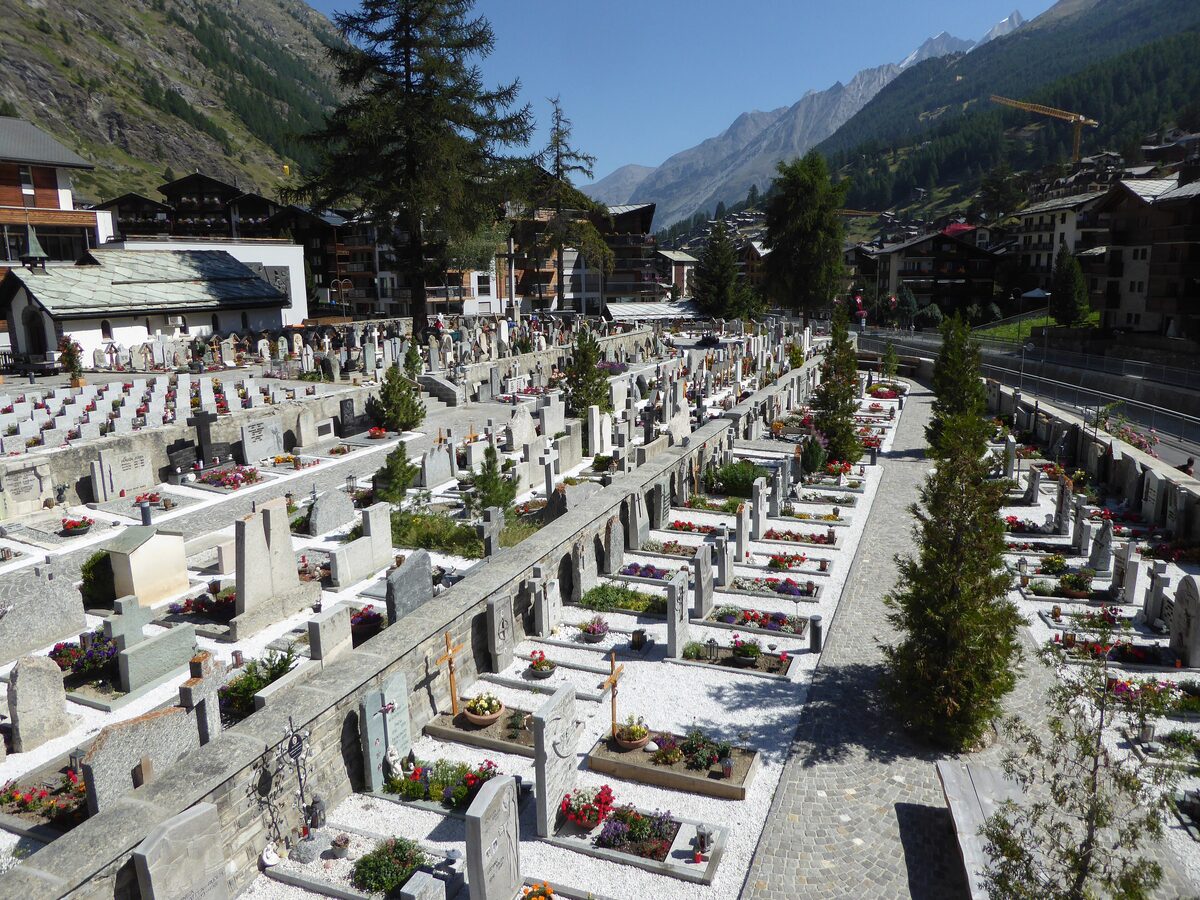 Graves with flowers in the Zermatt cemetery on a summer day, with chalets and mountain slopes behind